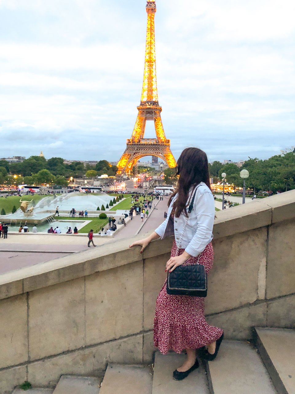 Woman in a white and red floral dress standing on the Trocadero stairs looking at the Eiffel Tower