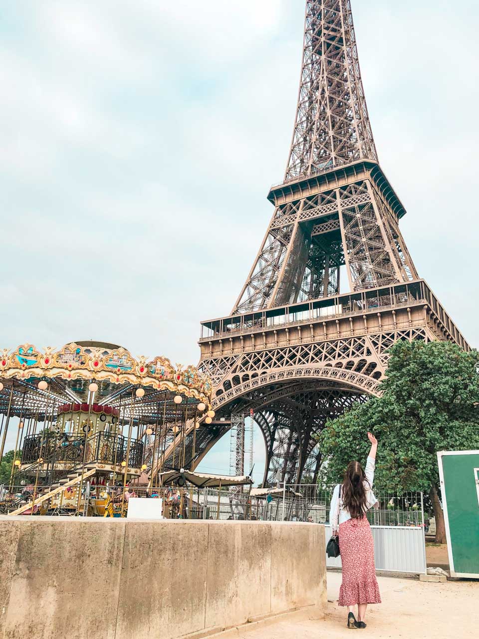 Woman throwing her right hand in the air as she is standing next to the Carousel of the Eiffel Tower