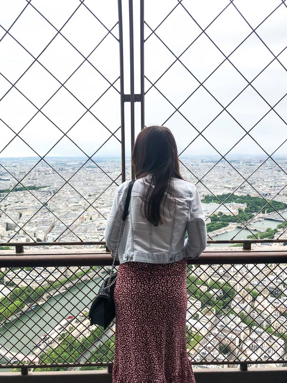 Woman in a denim jacket leaning against the ledge of the Eiffel Tower observation deck