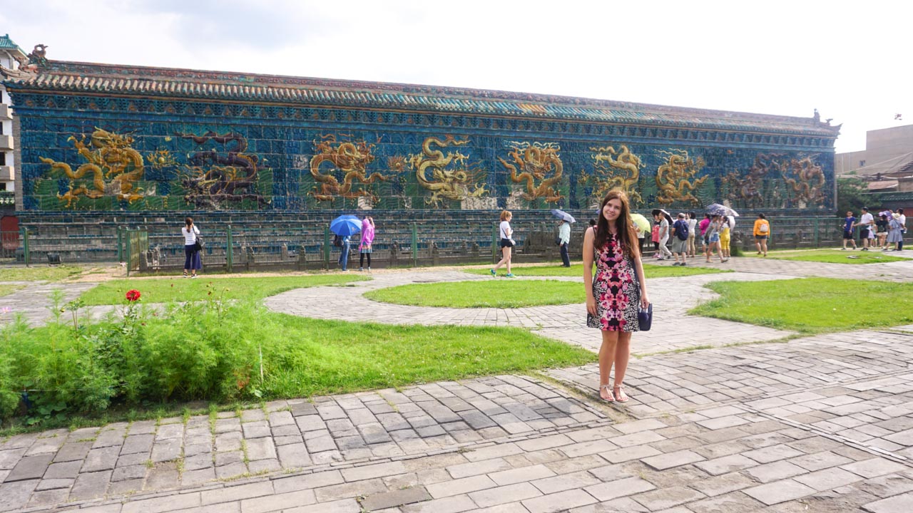 Smiling woman in a floral dress standing in front of the Nine-Dragon Wall in Datong, Shanxi