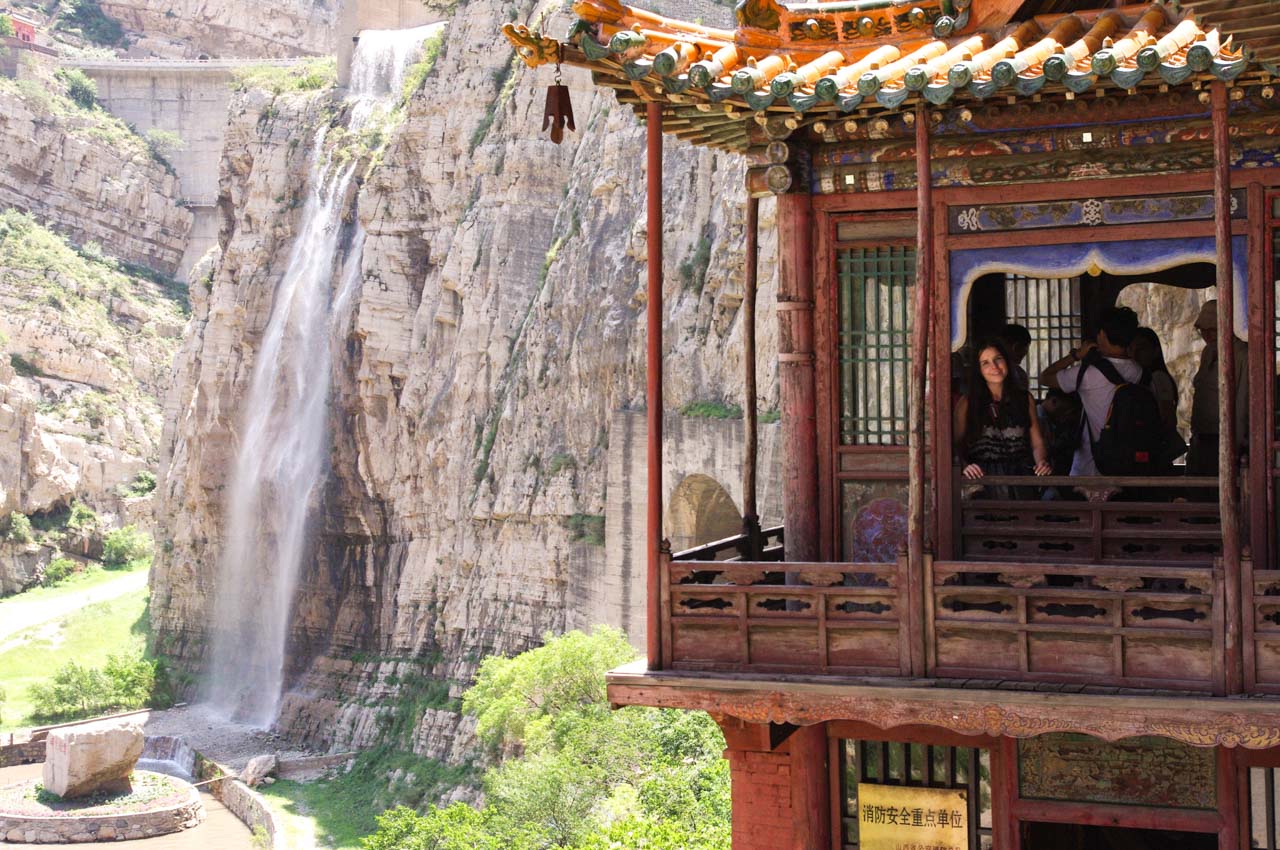 A woman standing inside a hall at the Hanging Temple in Datong with a waterfall in the background