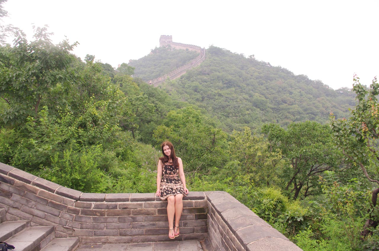 Smiling woman sitting on the Great Wall of China with a fog-covered section of the wall behind her