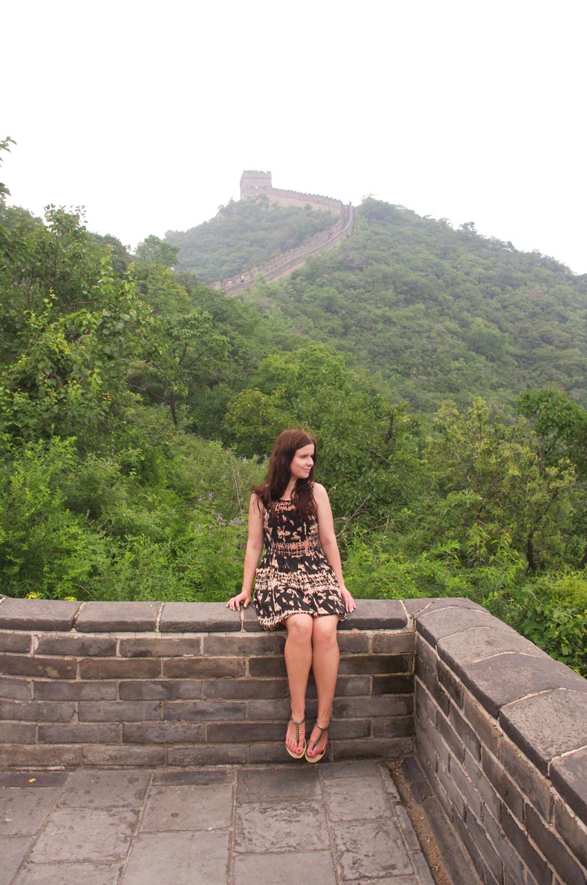 Woman sitting on the Great Wall of China with a fog-covered section of the wall behind her