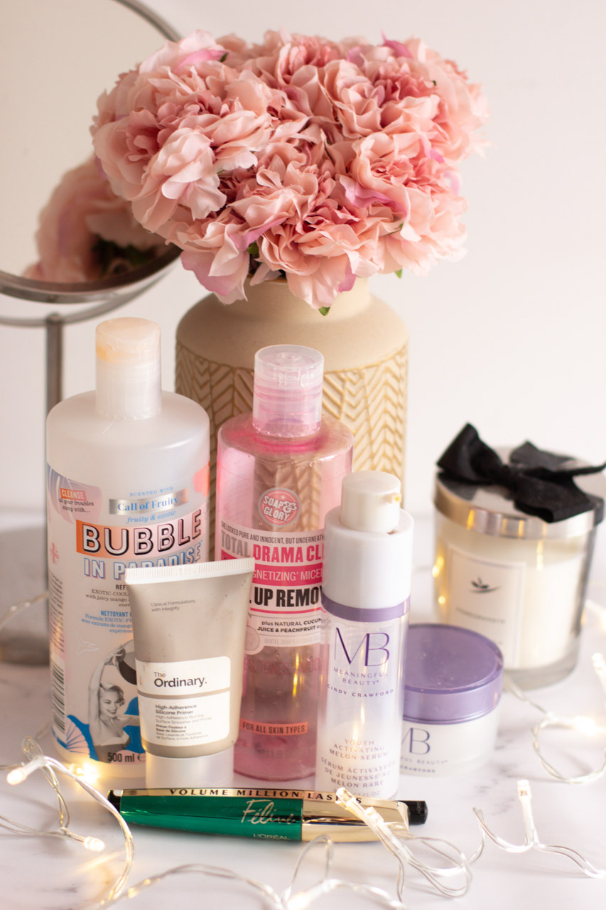 Empty beauty products on a marble desk in front of a vase with pink peonies and a makeup mirror