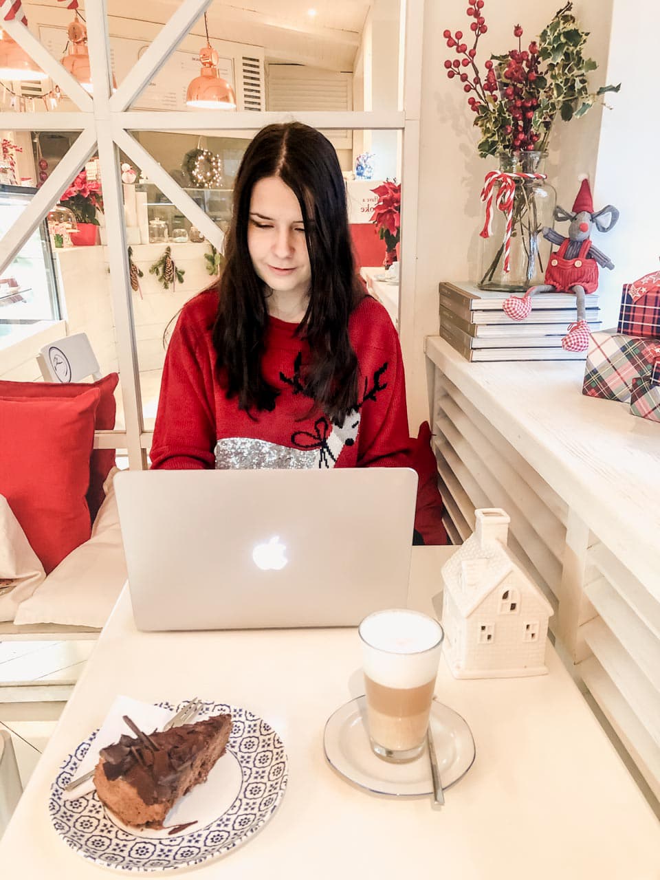 Girl typing something on her MacBook Air with a piece of cake and a cup of coffee placed beside her