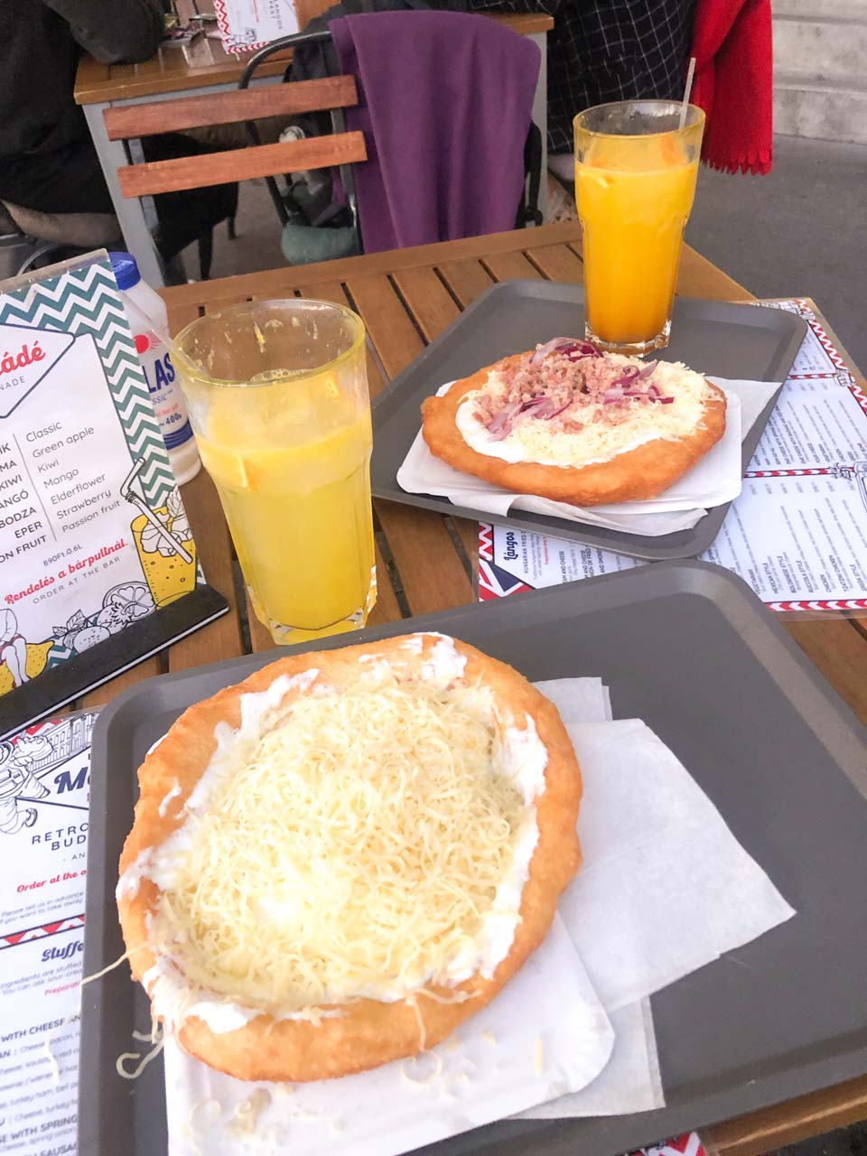 Two glasses of lemonade and two different kinds of lángos on a table