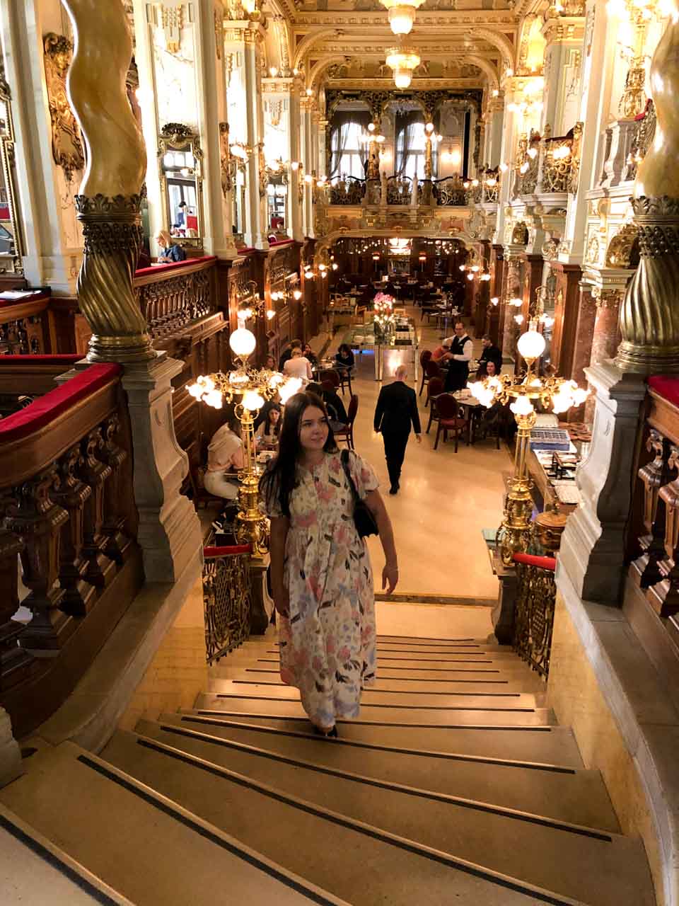 A girl in a maxi dress walking up the stairs inside the New York Café in Budapest