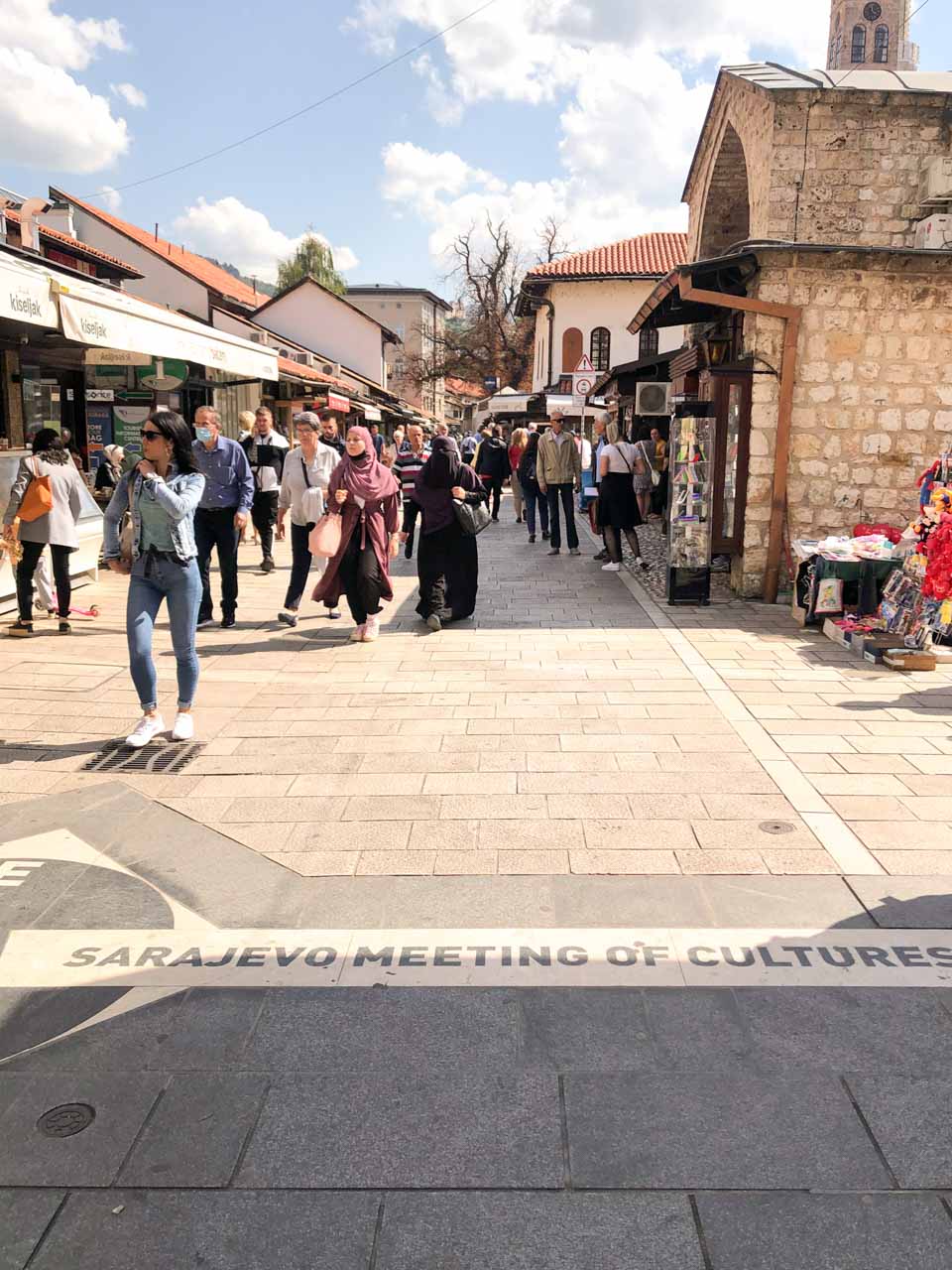 People walking next to the Sarajevo Meeting of Cultures mark on Ferhadija Street