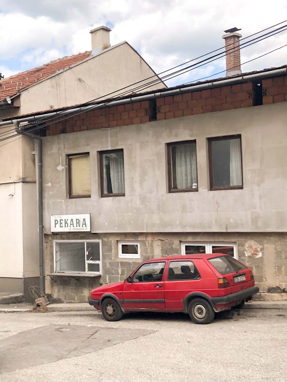 An old red car parked outside a bakery in Sarajevo