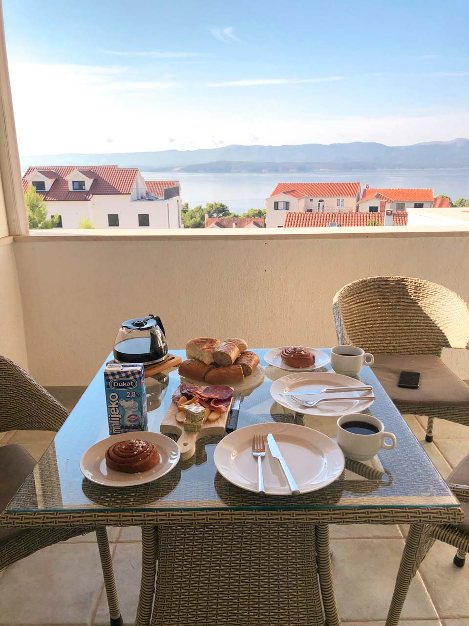 A table on an open terrace filled with different kinds of breakfast foods with the Adriatic Sea in the background