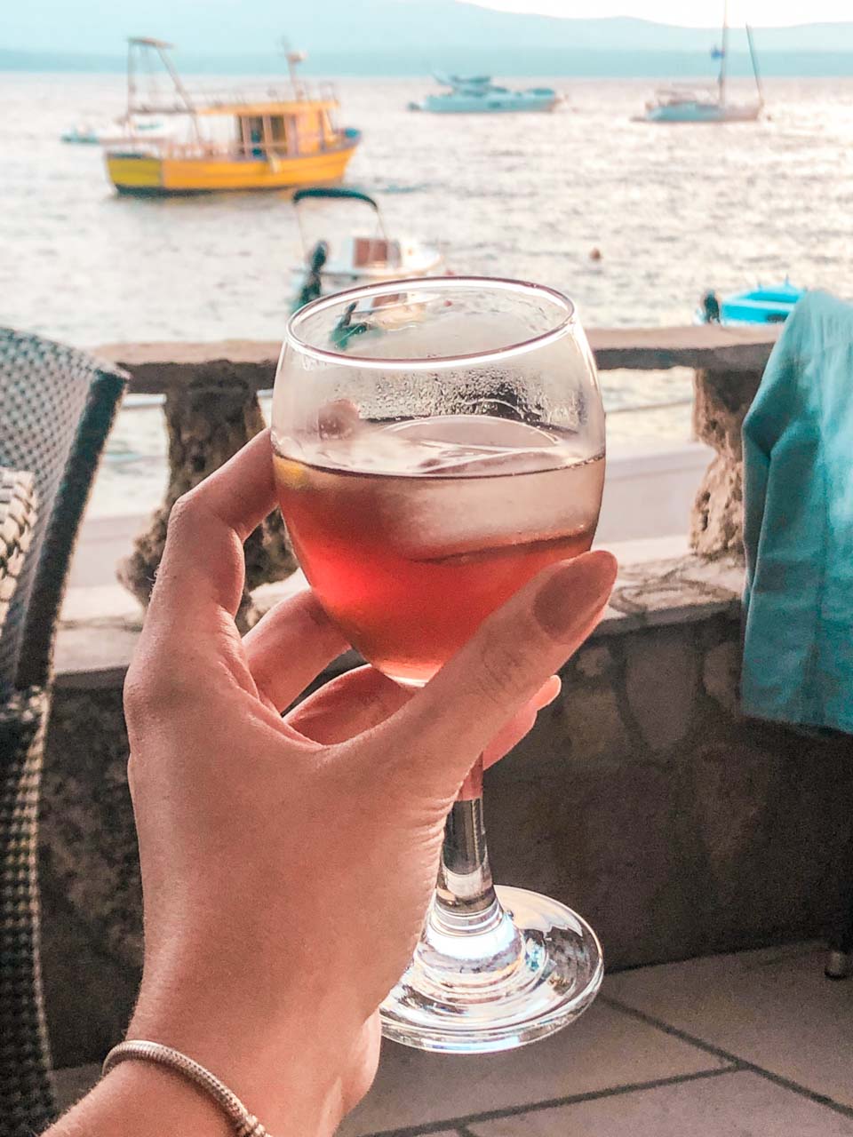 Female hand holding a glass of Prošek wine with boats on the Adriatic Sea in the background