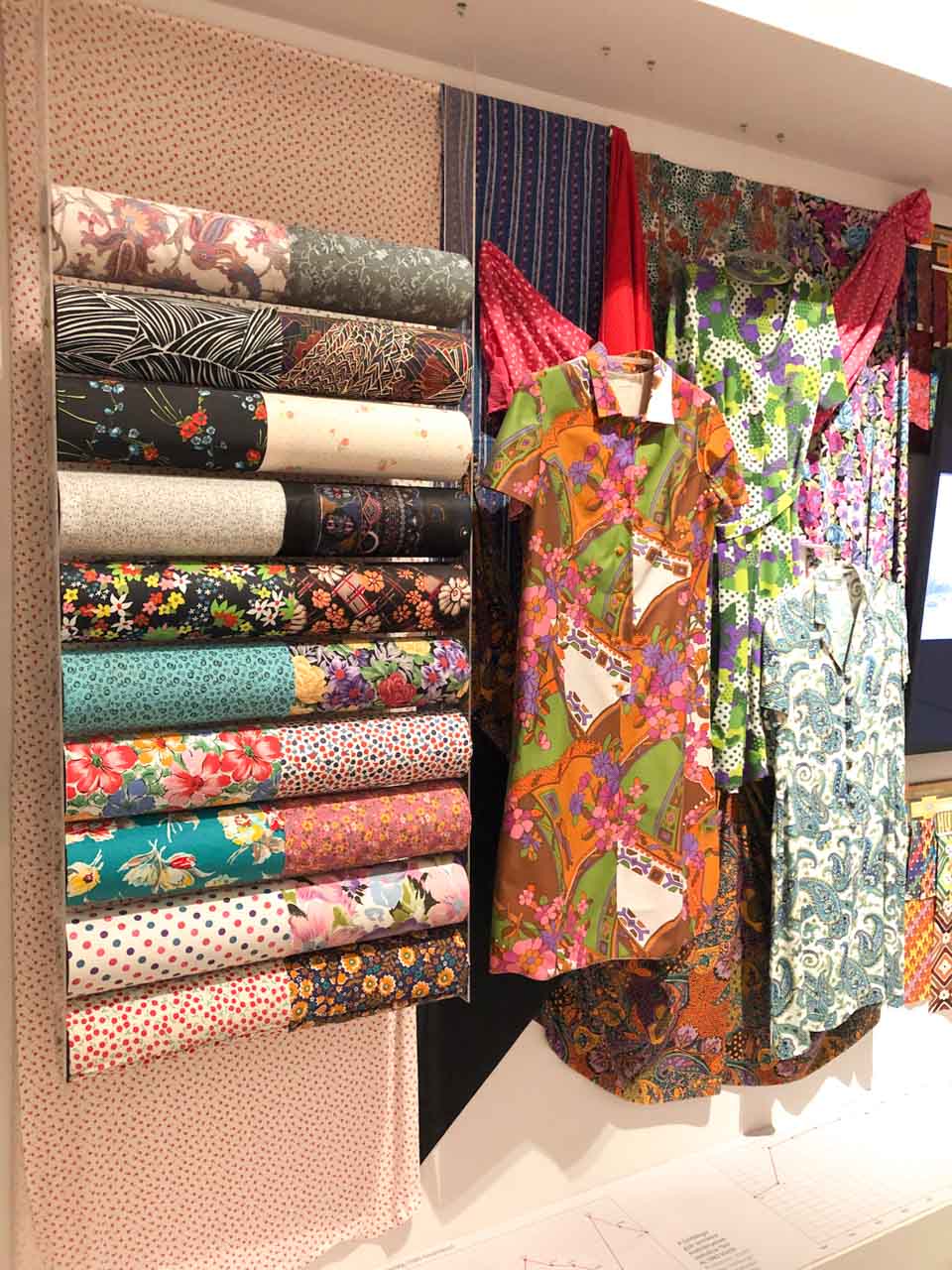Rolls of printed fabric next to some hanging printed garments