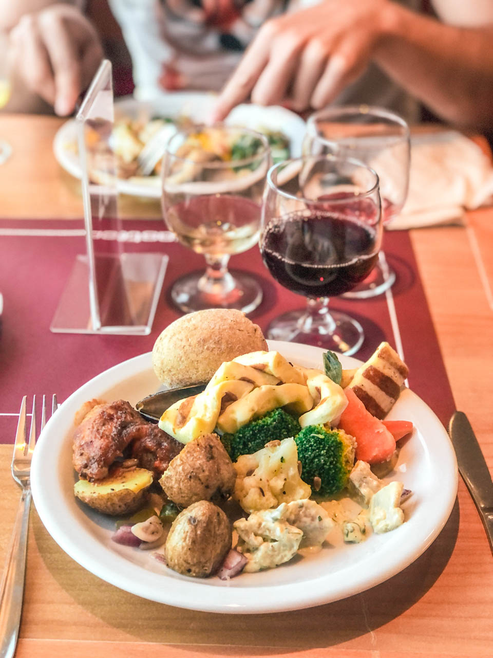 A close-up photo of a plate filled with different kinds of meats and vegetables next to three wine glasses