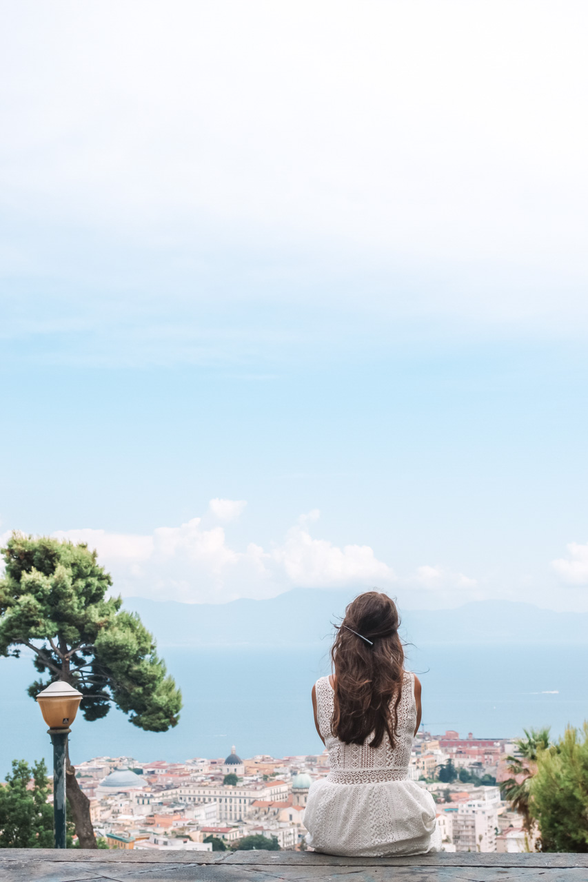 A girl in a white lace dress sitting on top of the stairs overlooking the Bay of Naples
