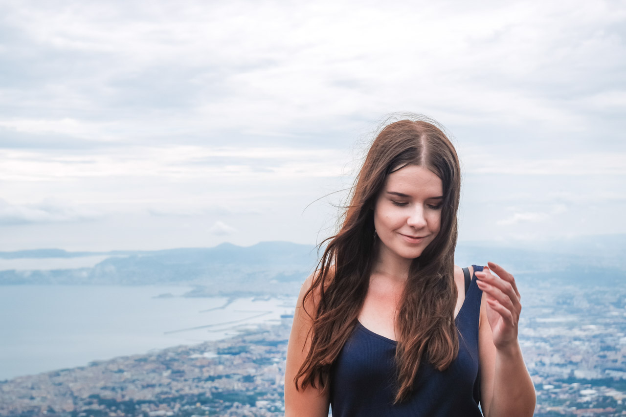 A girl standing on the summit of Mount Vesuvius with a view of the Bay of Naples behind her