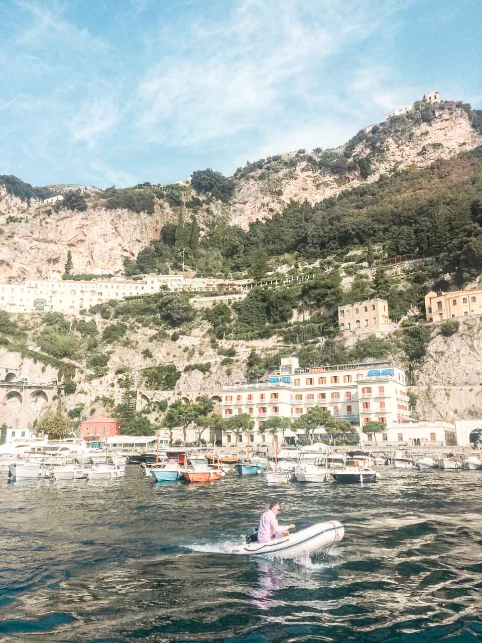 A man on a fishing boat in Positano with the hillside houses and the mountains in the background