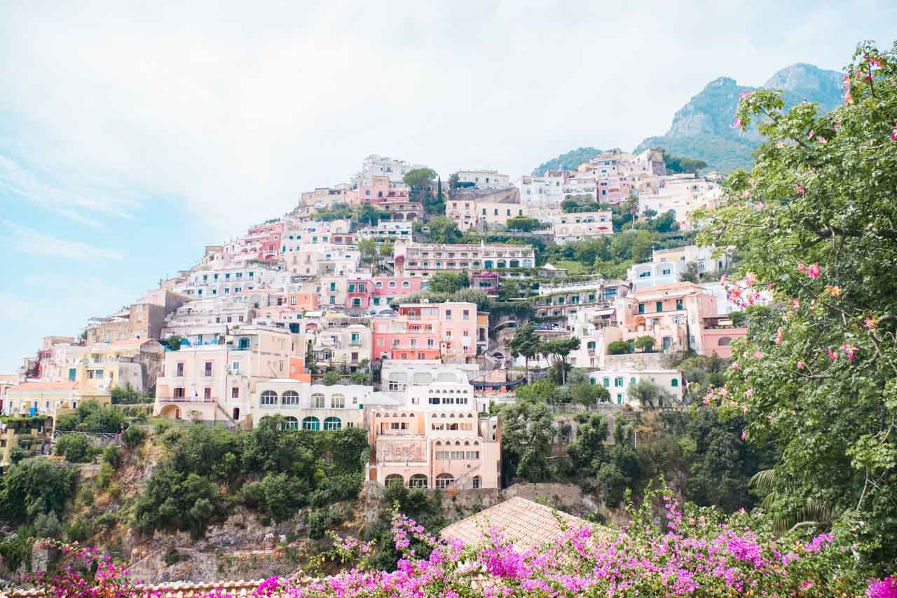 Pastel hillside houses in Positano, Italy surrounded with green bushes and fuchsia flowers