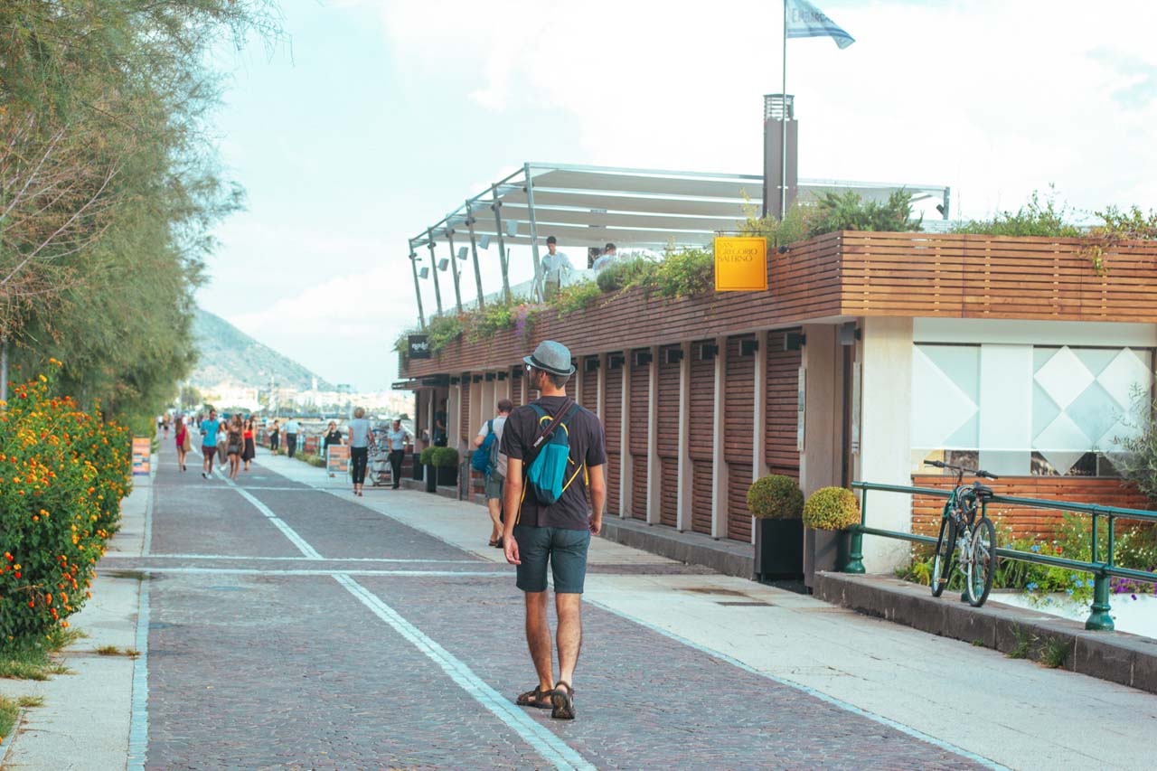 A man with a backpack walking alongside the Lungomare Trieste promenade in Salerno, Italy