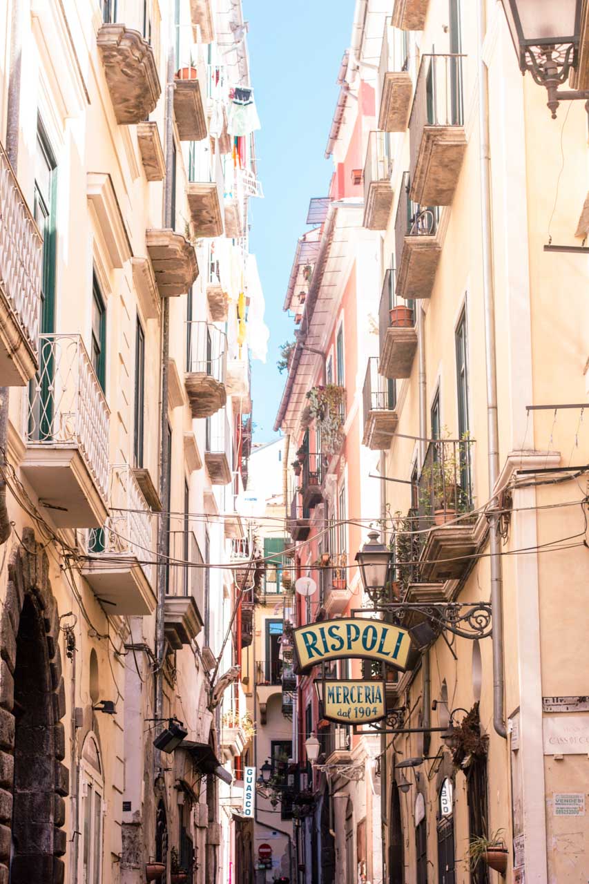 An alley with pastel buildings and a vintage shop sign in Salerno, Italy