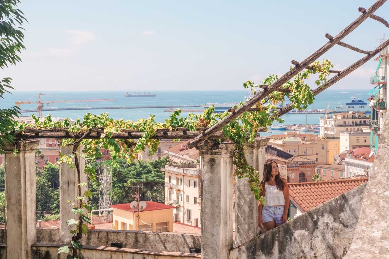 Girl looking up with vines hanging above her head and the Bay of Salerno in the background