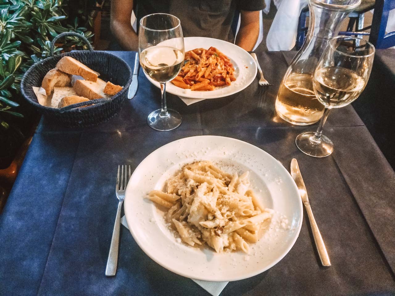 Two plates of pasta, wine glasses and a basket of bread on a table at Osteria del Campo in Salerno