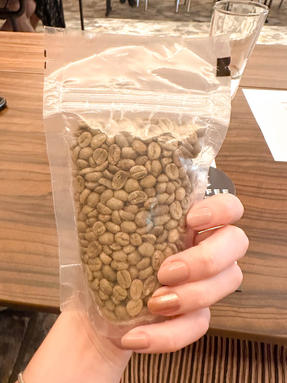 A woman's hand holding a bag of unroasted coffee beans