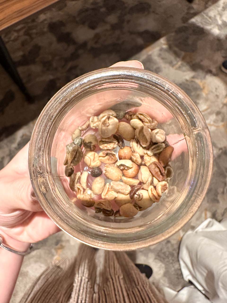 A woman's hand holding a jar with defective coffee beans