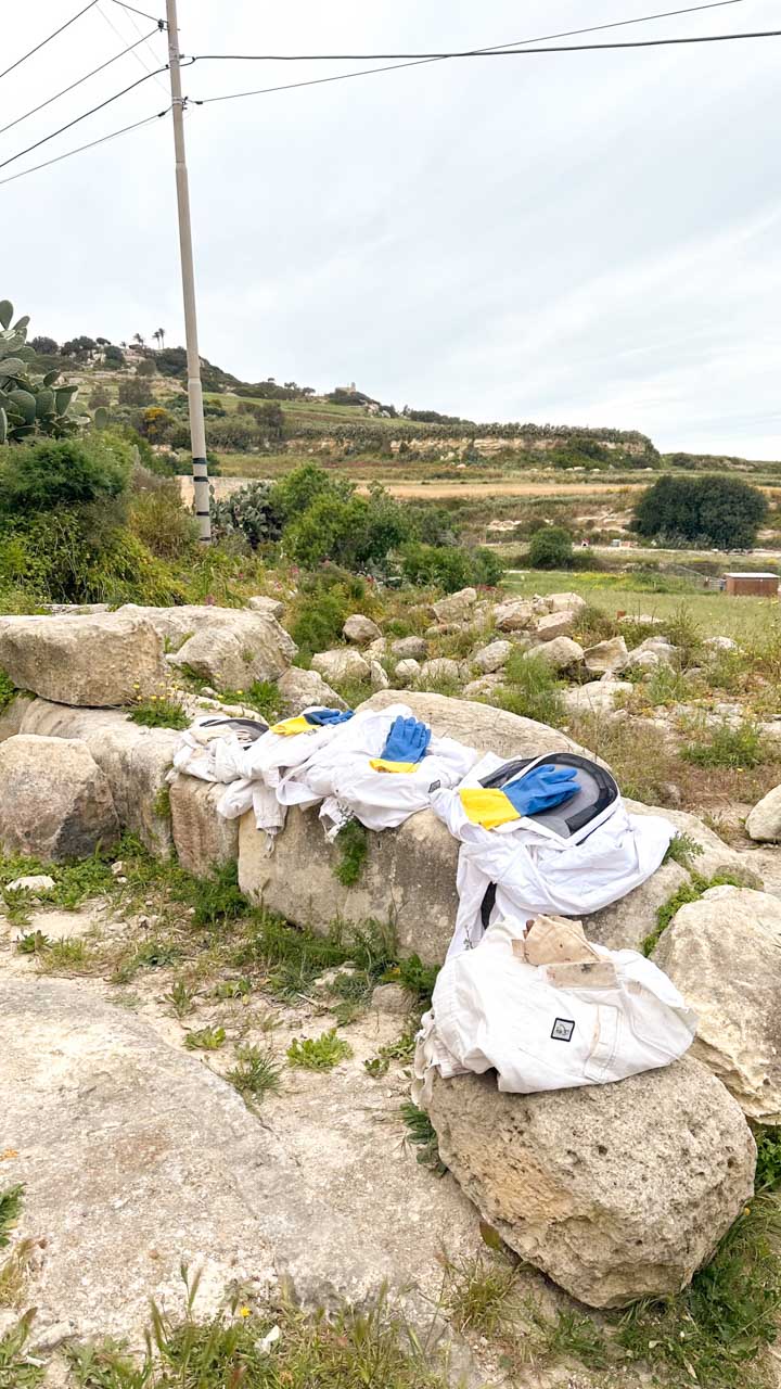 Beekeeper's suits and gloves placed on rocks in the Maltese countryside