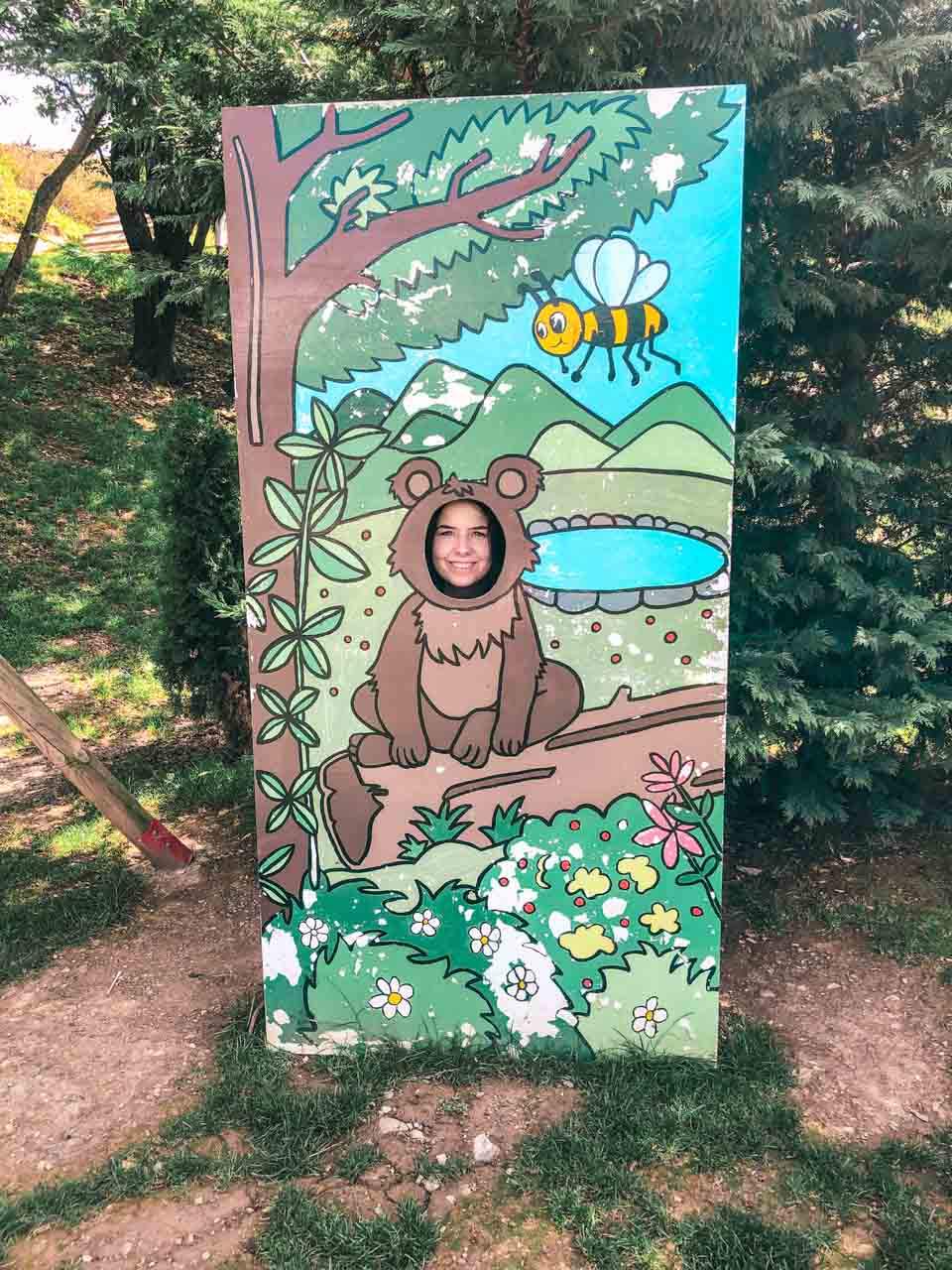 Girl sticking her face through the hole of a photo stand-in with a brown bear and a bee painted on it
