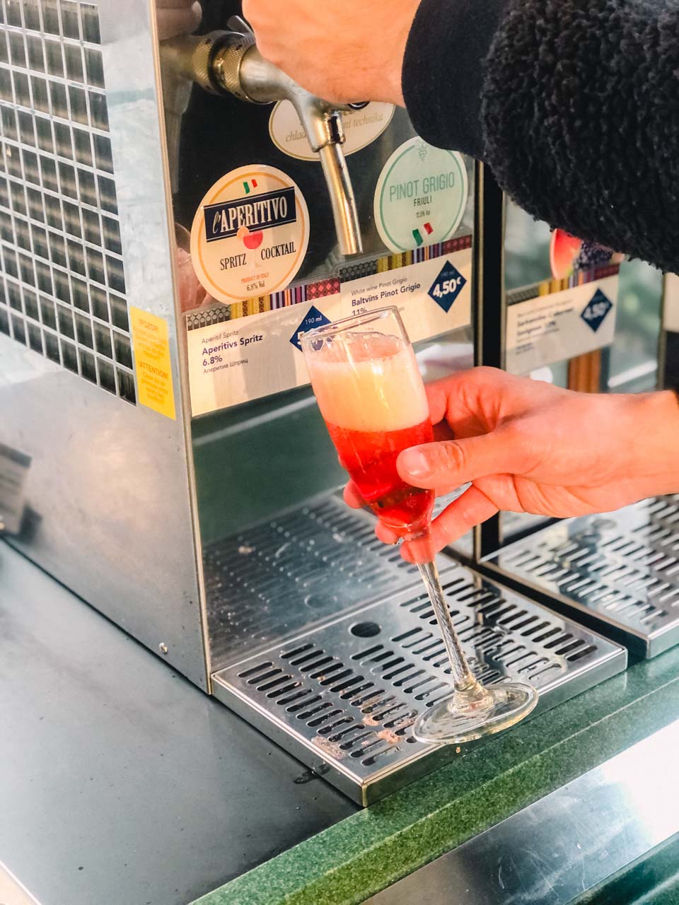 A man pouring a glass of aperitivo at a self-serve station inside a Lido restaurant in Riga Old Town