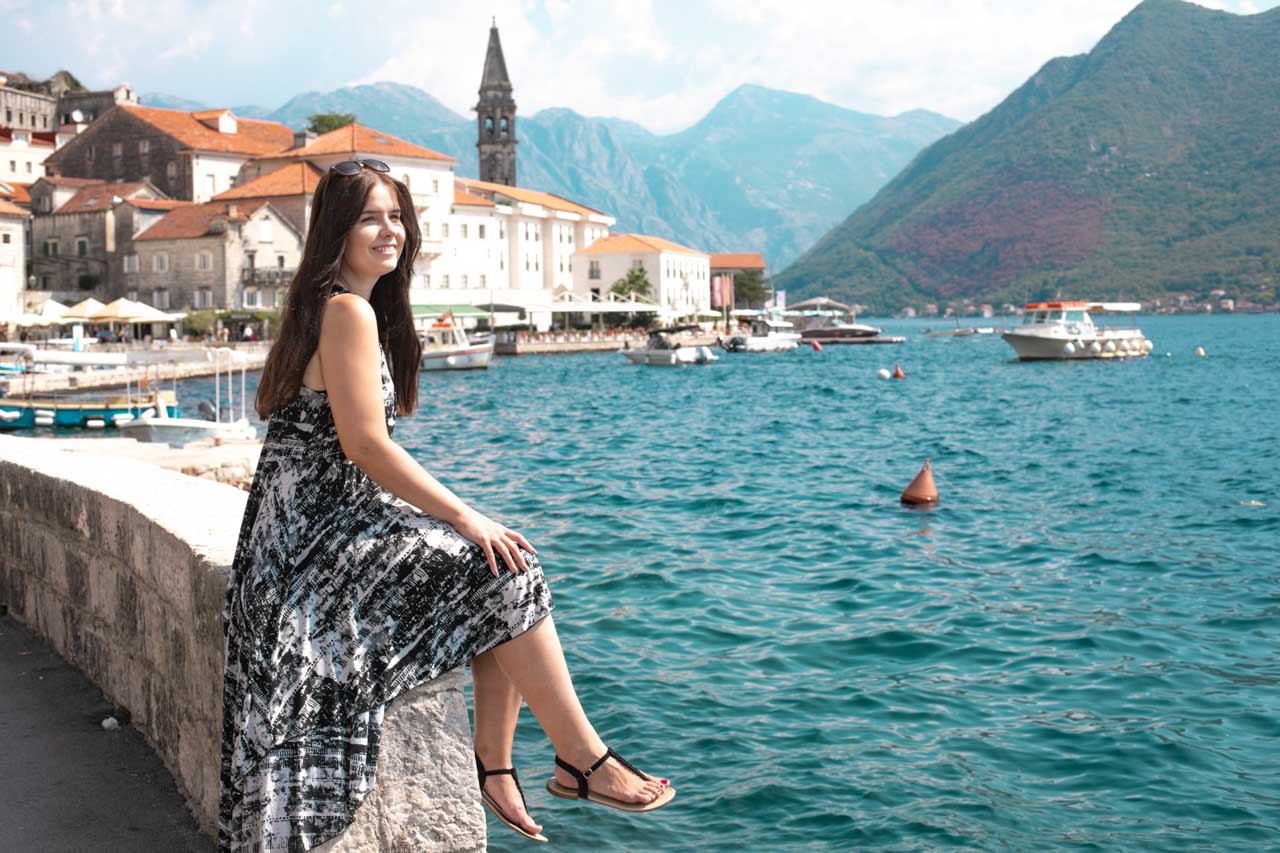 Girl in a black and white midi dress sitting on a stone wall on the Perast waterfront