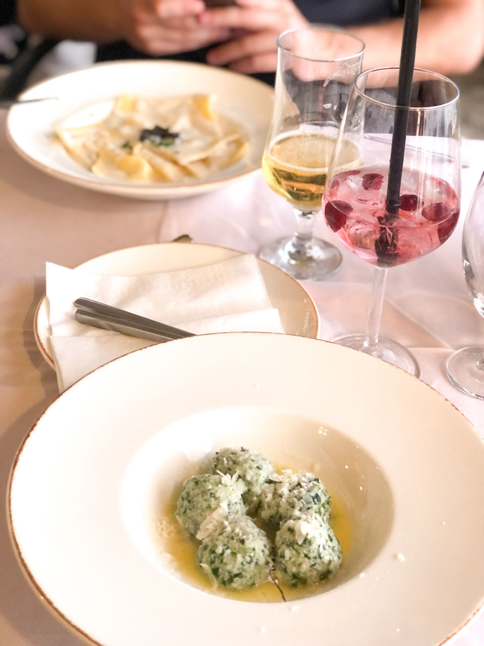 Gnudi Toscani in sage sauce, ravioli with shrimps, foie gras, and truffles, and two cocktails on a table