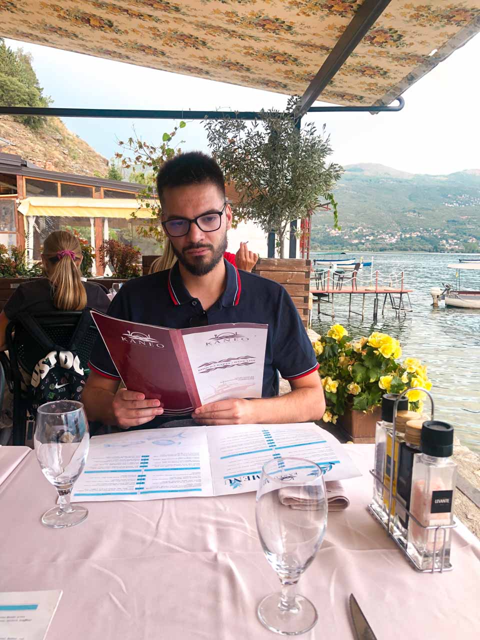 A man in a navy polo shirt reading the menu on the terrace of the Kaneo restaurant in Ohrid, North Macedonia