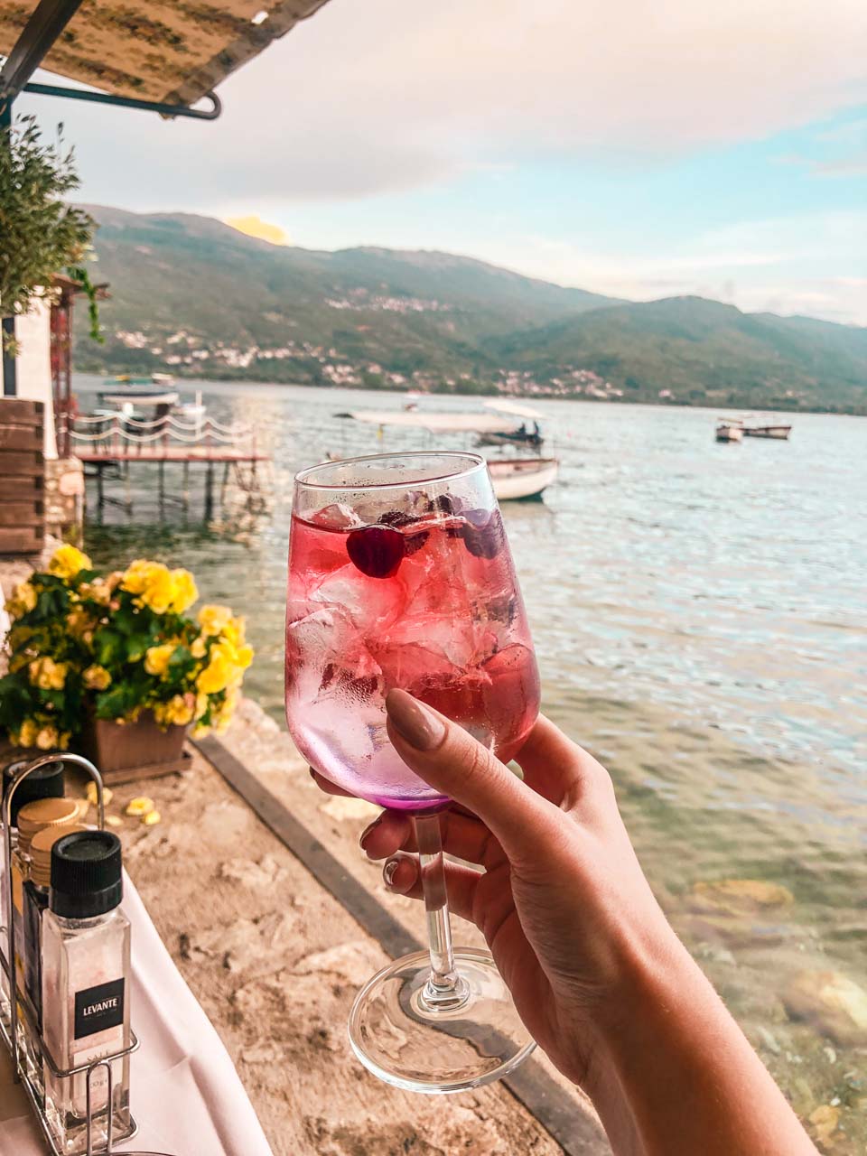 Woman holding up a pink cocktail against the backdrop of Lake Ohrid