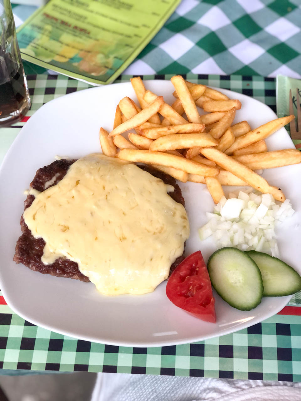 Meat patty with cheese on top and a side of chips and vegetables