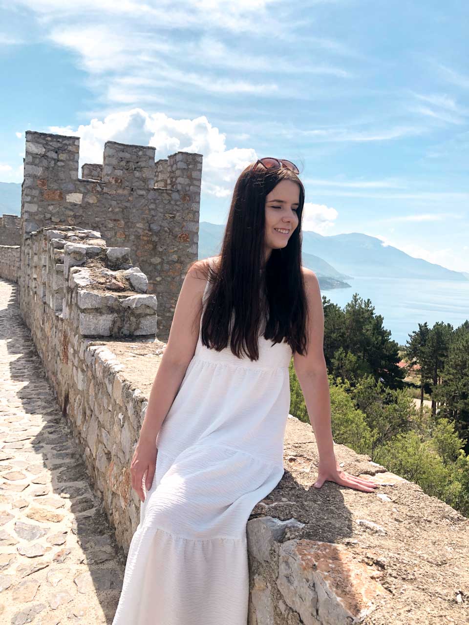 Woman in a white maxi dress leaning against the ledge of Samuel’s Fortress in Ohrid, North Macedonia