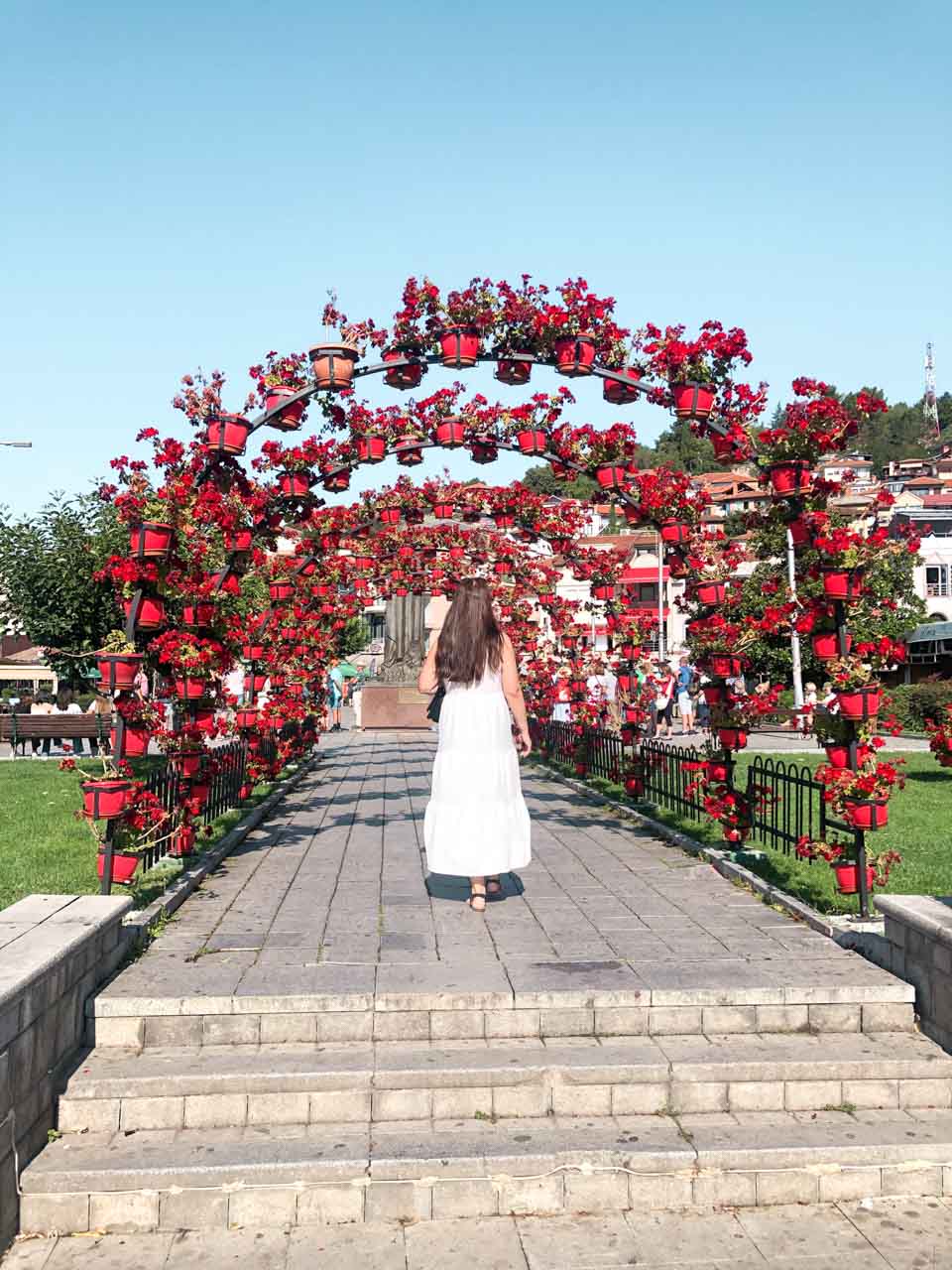 Woman in a white maxi dress walking under the flower arch in Ohrid, North Macedonia