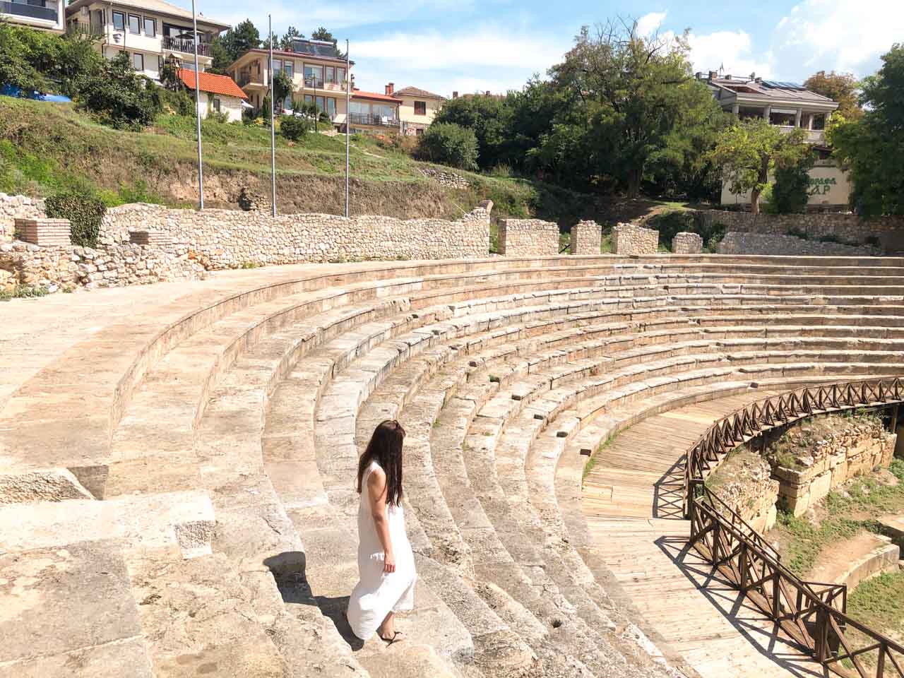 Brunette in a white maxi dress walking down the steps of the Ancient Theatre of Ohrid