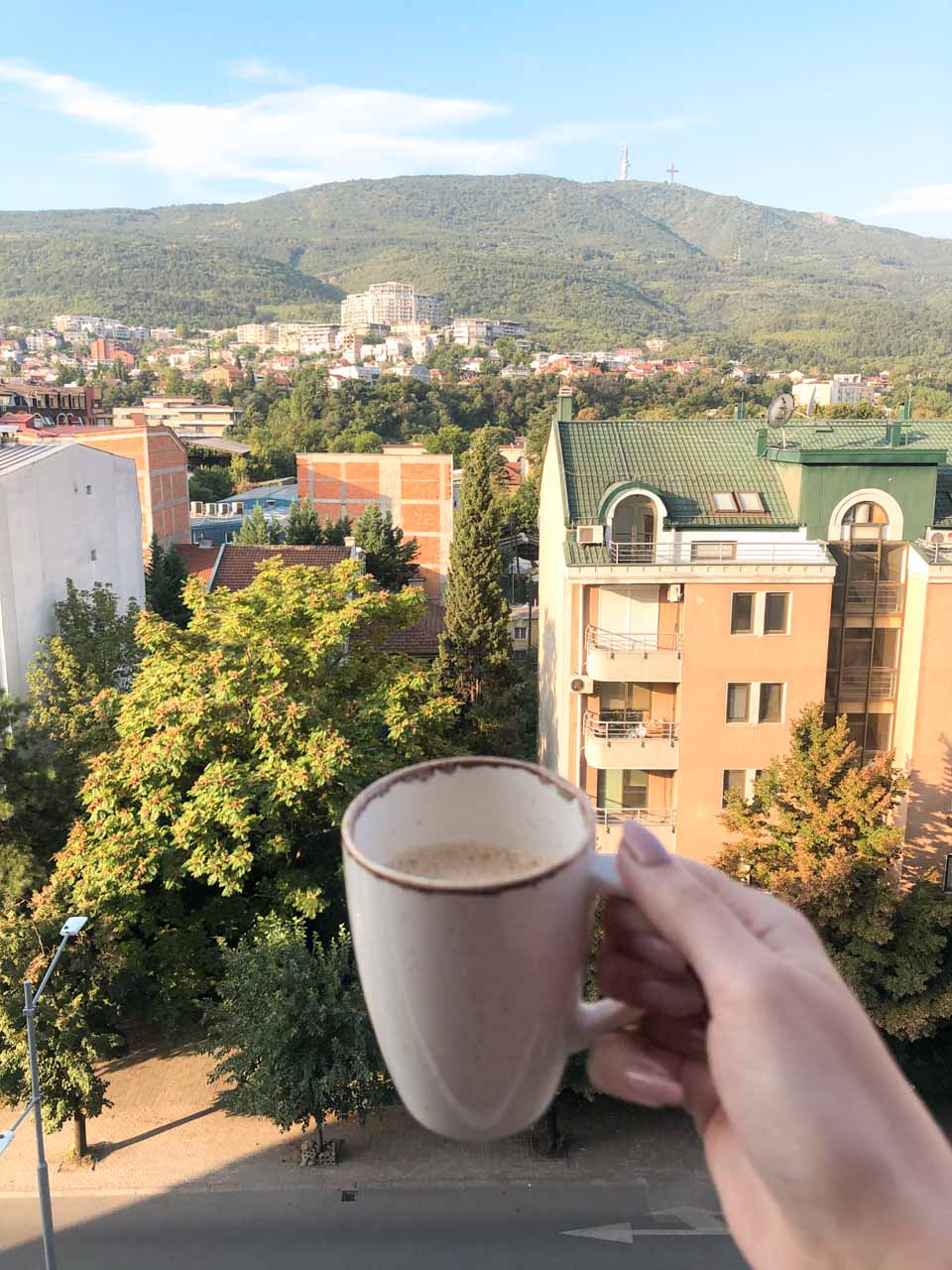 A woman holding up a cup of coffee with the Vodno Mountain in the background
