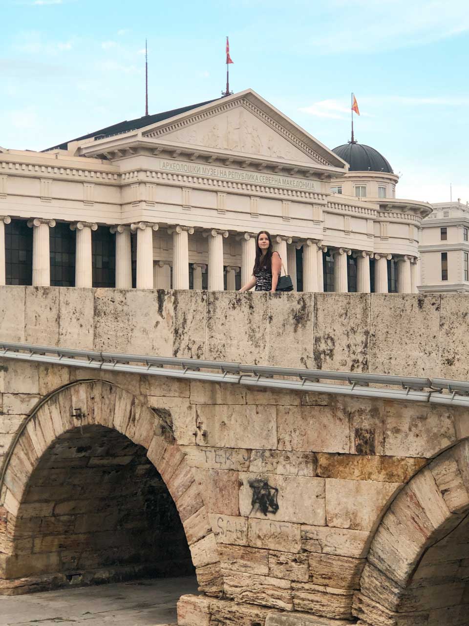 Woman standing on the Stone Bridge in Skopje with the Archaeological Museum of the Republic of Macedonia behind her