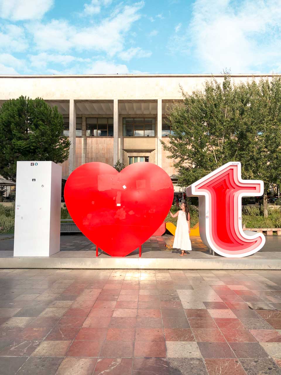 Girl in a white maxi dress standing next to the I love T symbol on Skanderbeg Square in Tirana