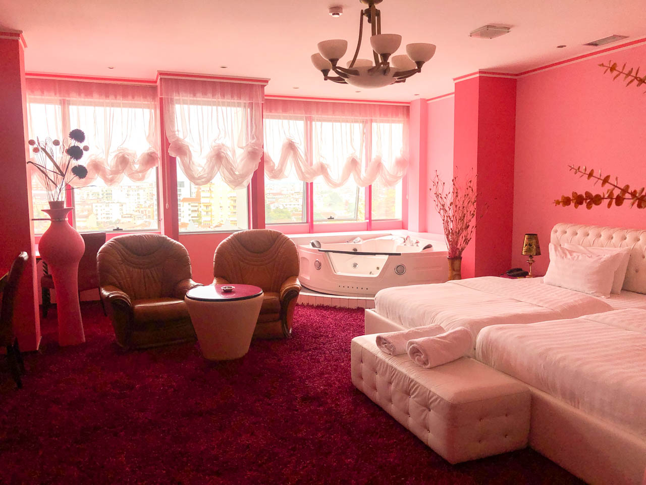 Pink hotel room with a white bed, a jacuzzi, and leather armchairs at the Rosa Blu hotel in Tirana, Albania