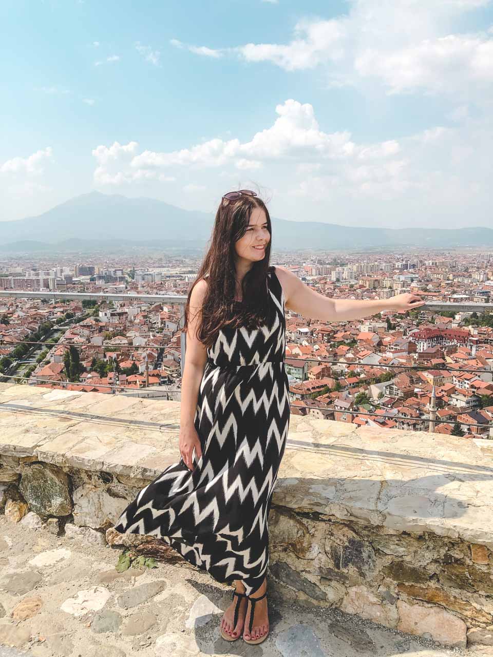 Brunette standing at the top of the Prizren Fortress with a panorama of the city behind her