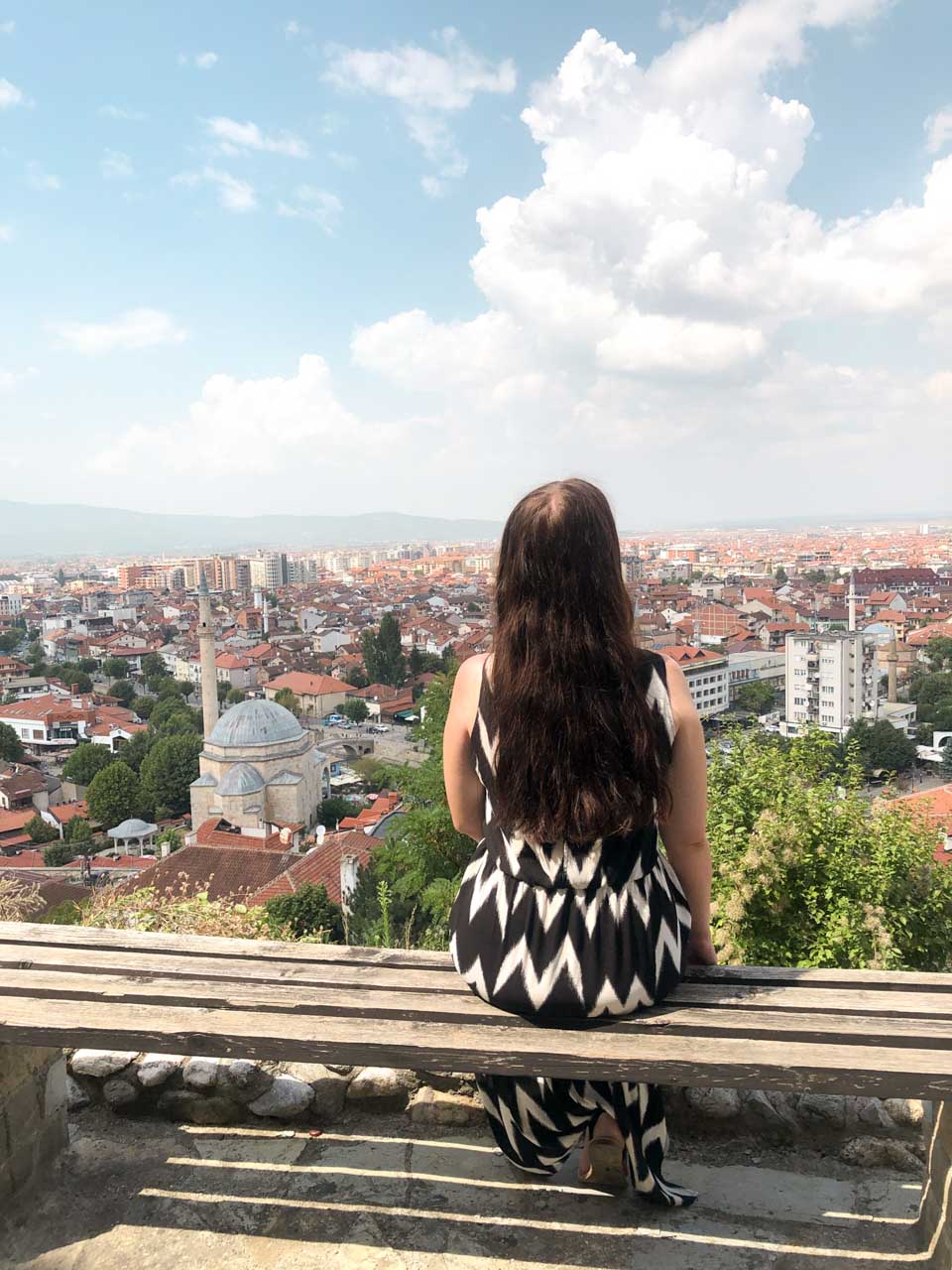 Woman in a black and white dress sitting on a bench overlooking the city of Prizren, Kosovo