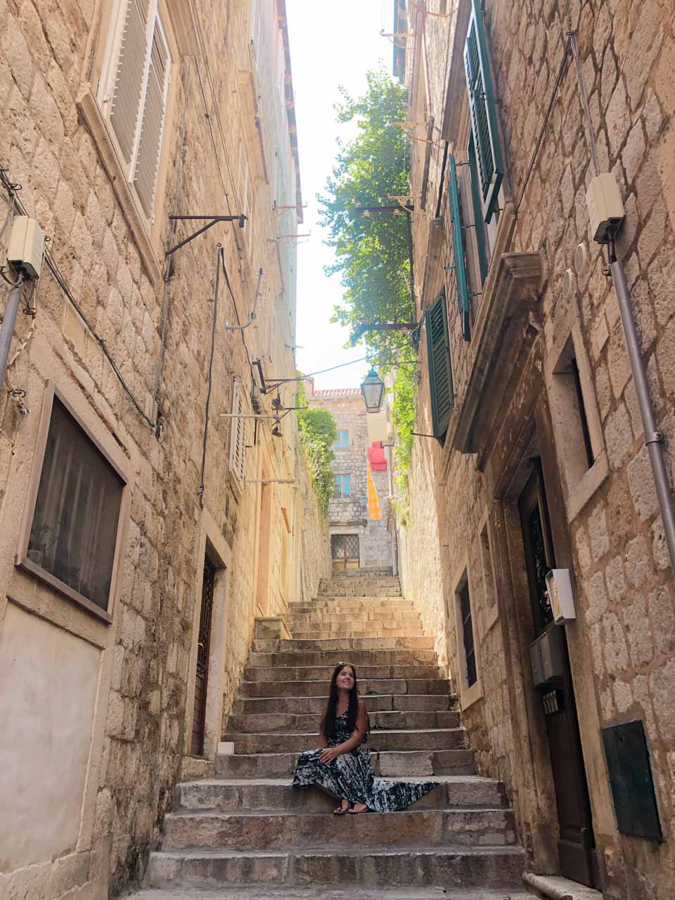 Woman in a black and white dress sitting on the stairs on Božidarevićeva street in Dubrovnik Old Town