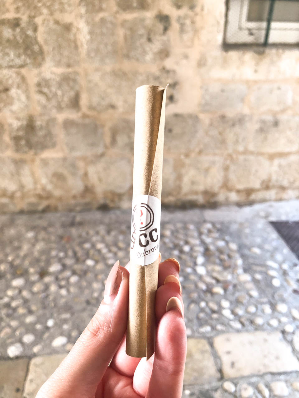 A girl holding up a rolled up Curious Card on a cobblestone street of Dubrovnik Old Town