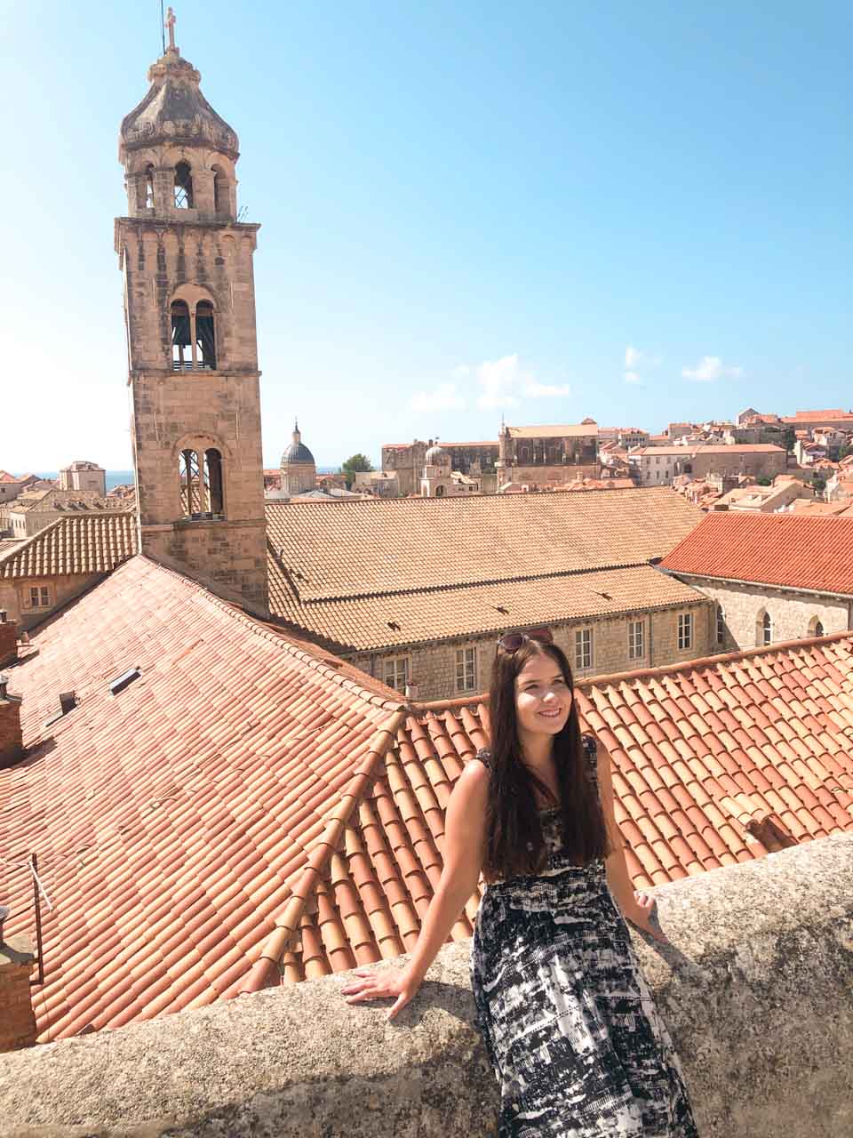 Smiling brunette leaning against the Dubrovnik City Walls with Dubrovnik Old Town in the background