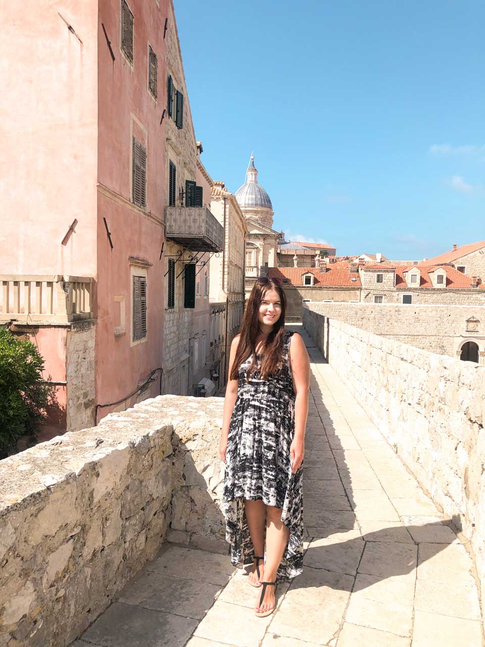 Woman in a black and white high-low dress standing on the Dubrovnik City Walls and smiling at the camera