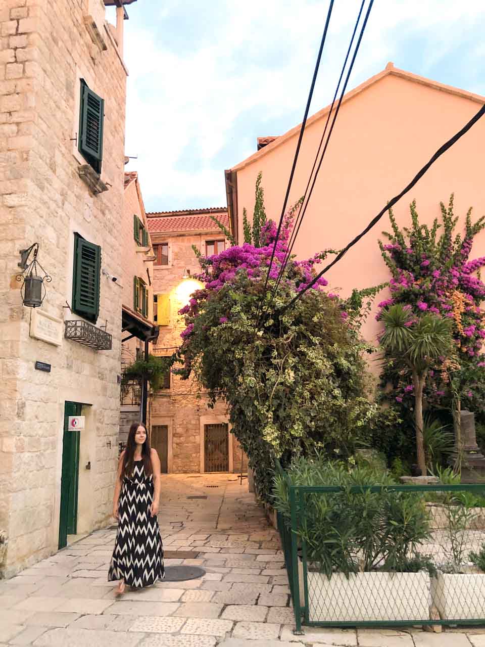 Woman in a black and white maxi dress walking past a building in Split Old Town draped with Bougainvillea
