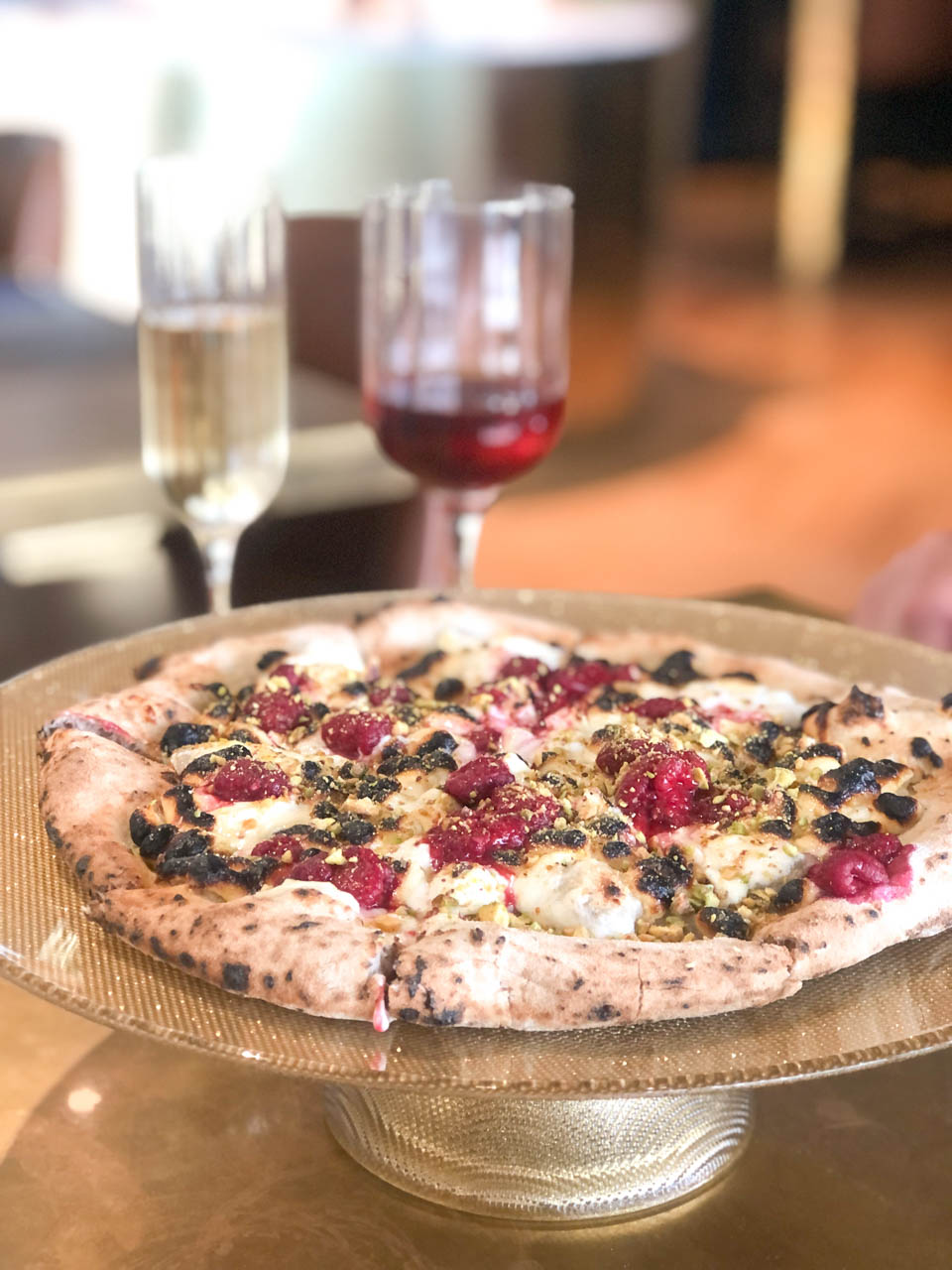 Slatkizza pizza with mozzarella, white chocolate, raspberries, and pistachios and two wine glasses on a table at Bokamorra in Split